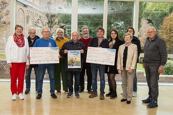 Antje Jolink (links), Pastor Klaus Winkel (hinten, Mitte) und Heinz Hetkamp (rechts) überreichen die Spendenschecks an Ewald Elsenbusch (von links), Ulrich Schindler, Christa Janßen, Winfried Niemarkt (alle von der Tafel), Manfred Mäteling, Maria Preizner, Angela Wendering-Ewald und Anneliese Oschilewski (alle Flüchtlingshilfe)