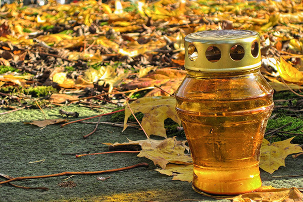 braungelbes Grablicht auf Grabplatte im Hintergrund braungelbes Laub