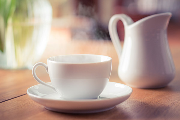 Tasse mit dampfendem Kaffee daneben ein Milchkännchen