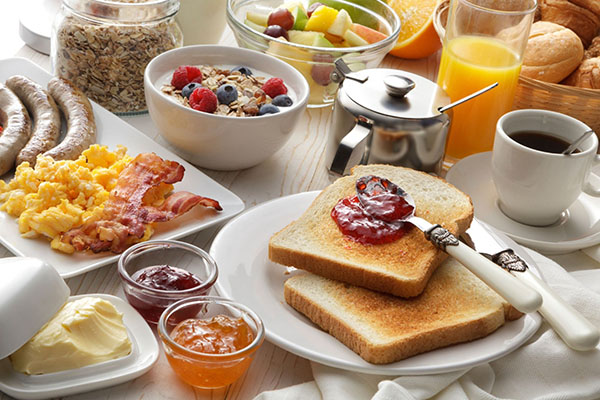 Symbolfoto: reichhaltiger Frühstückstisch mit Toastbrot, Kaffee, Saft, Müsli, Rührei und Speck